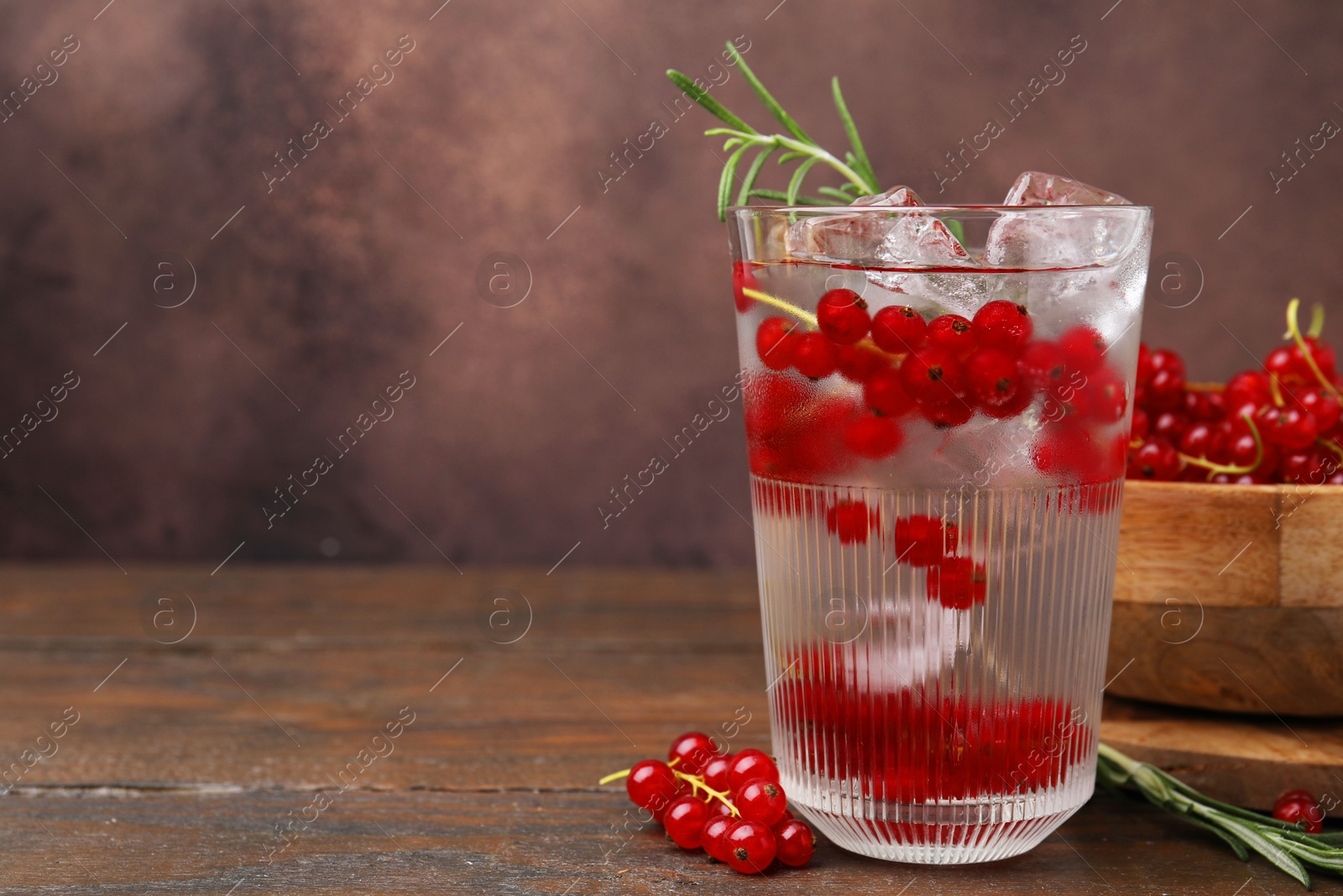 Photo of Refreshing water with red currants and rosemary in glass on wooden table, space for text