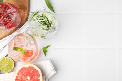 Different refreshing drinks in glasses on white tiled table, flat lay. Space for text