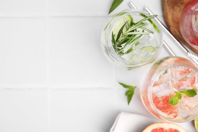 Photo of Different refreshing drinks in glasses on white tiled table, flat lay. Space for text