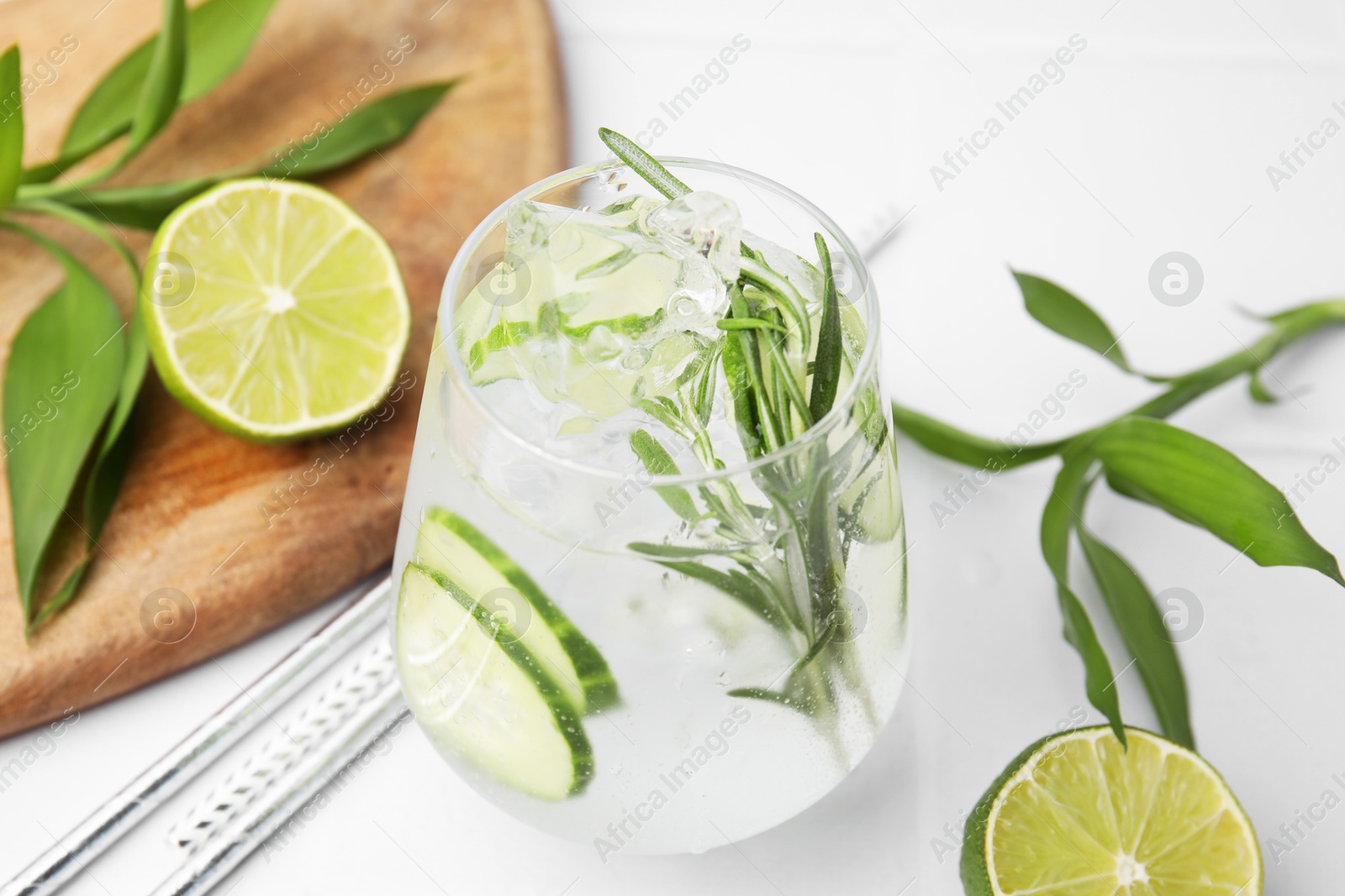 Photo of Refreshing water with cucumber and rosemary in glass on white tiled table, closeup