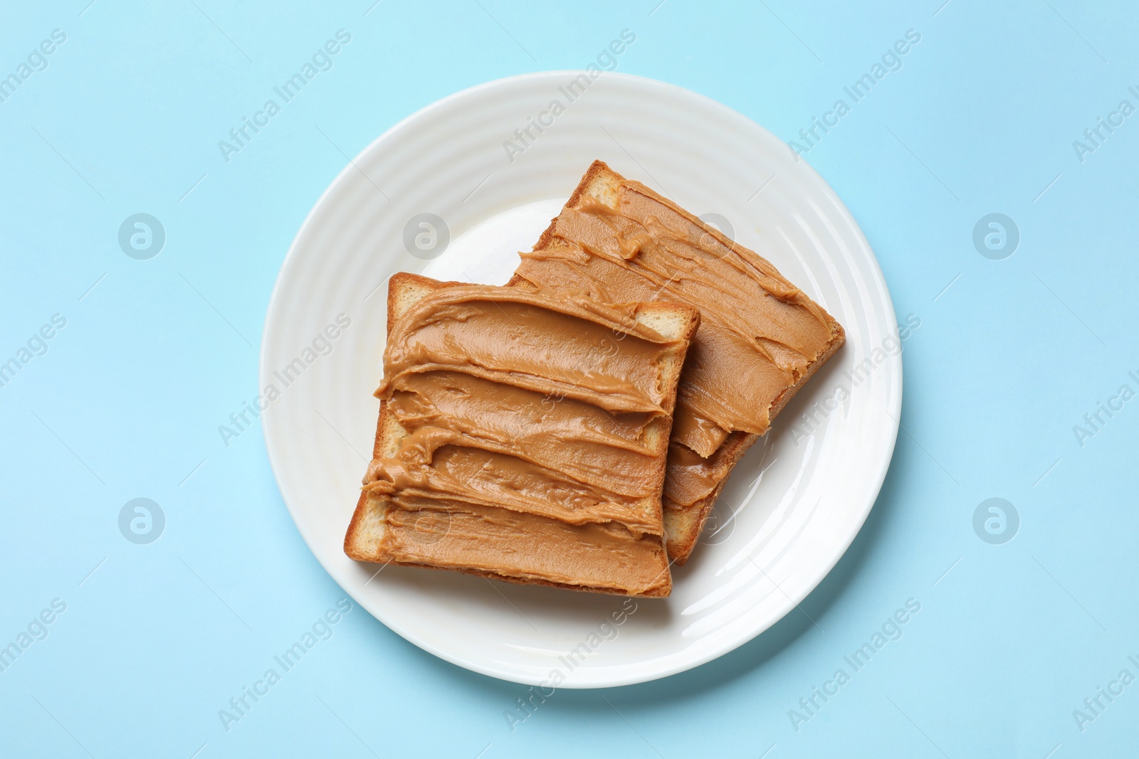 Photo of Delicious sandwiches with peanut butter on light blue table, top view