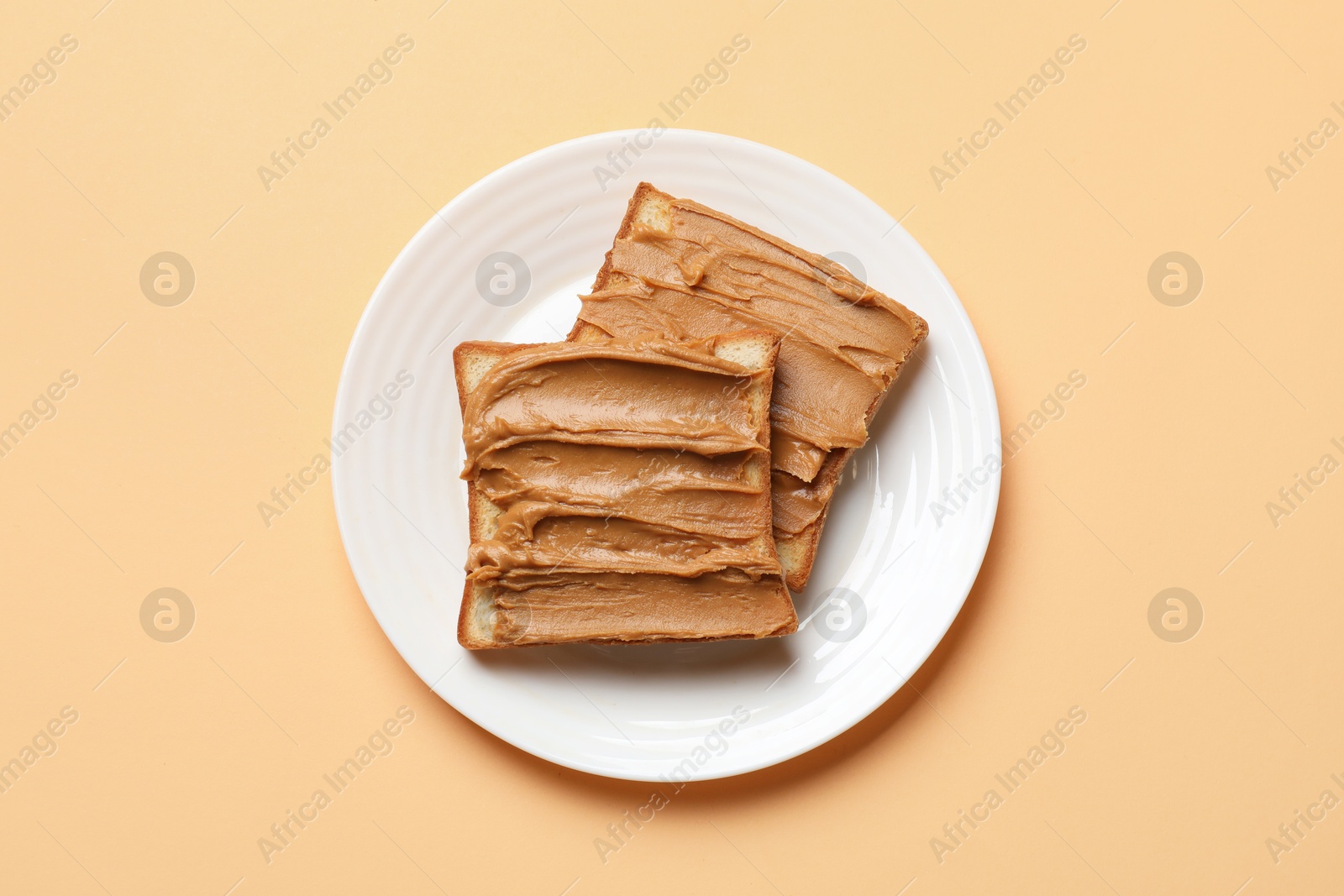 Photo of Delicious sandwiches with peanut butter on pale orange table, top view