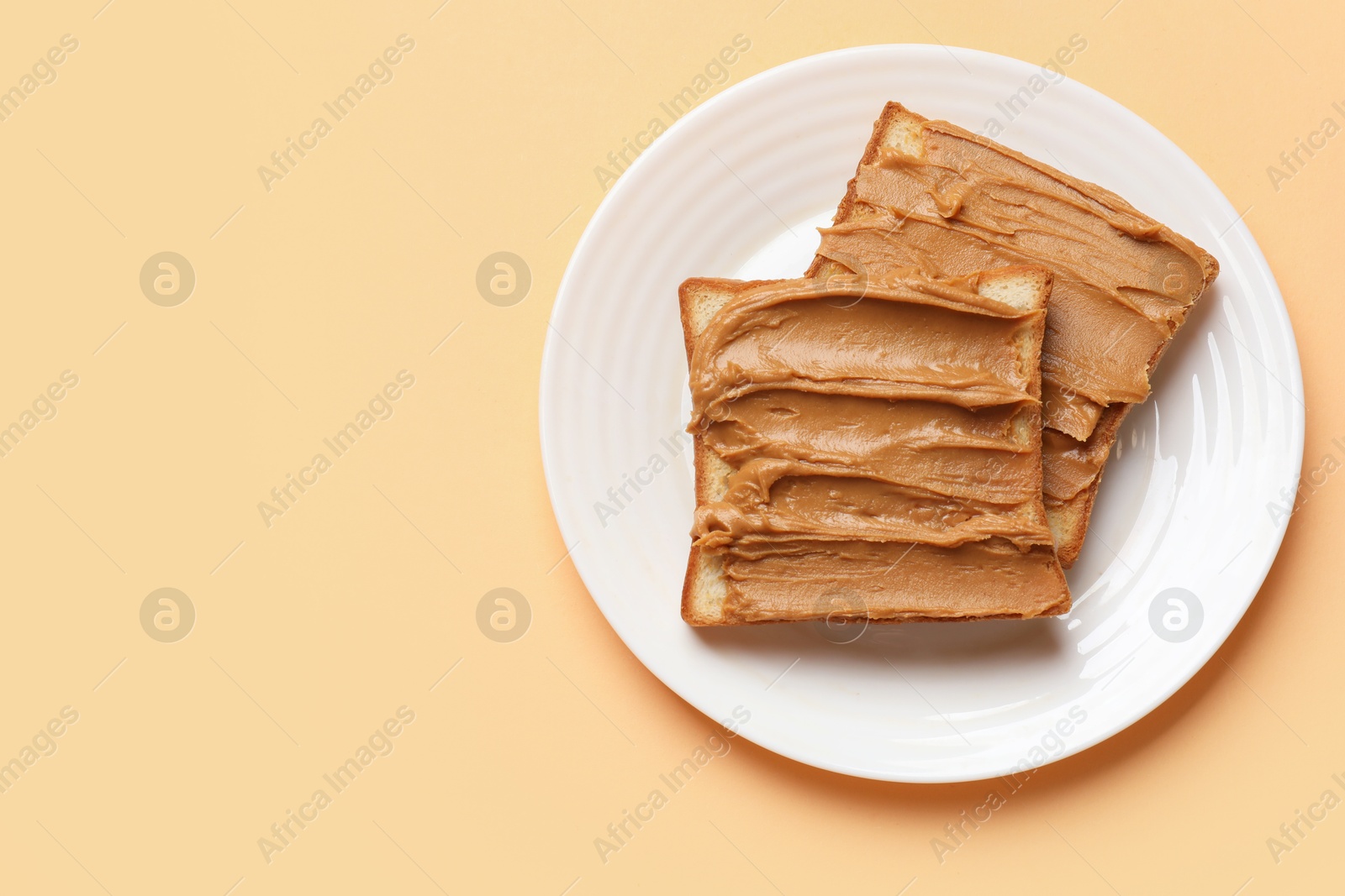 Photo of Delicious sandwiches with peanut butter on pale orange table, top view. Space for text