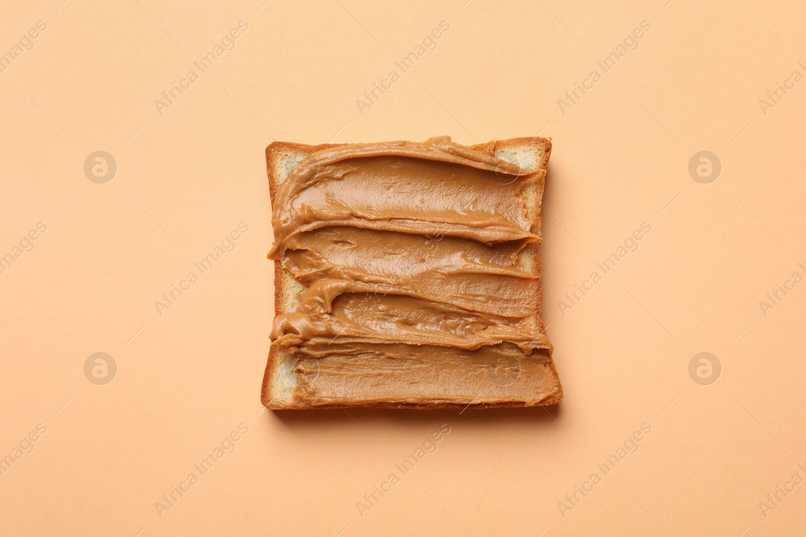 Photo of Delicious sandwich with peanut butter on pale orange table, top view