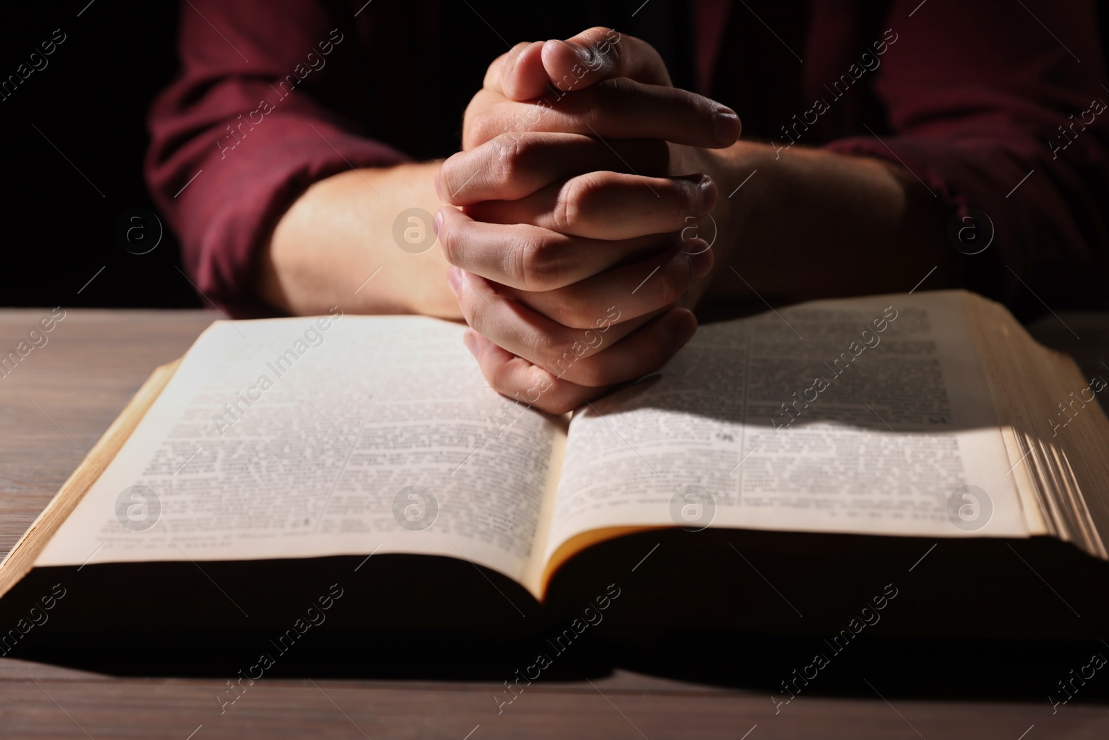 Photo of Man with Bible praying at wooden table, closeup