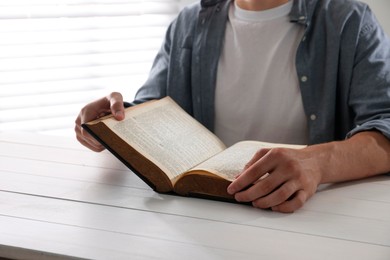 Photo of Man with Bible at white wooden table, closeup