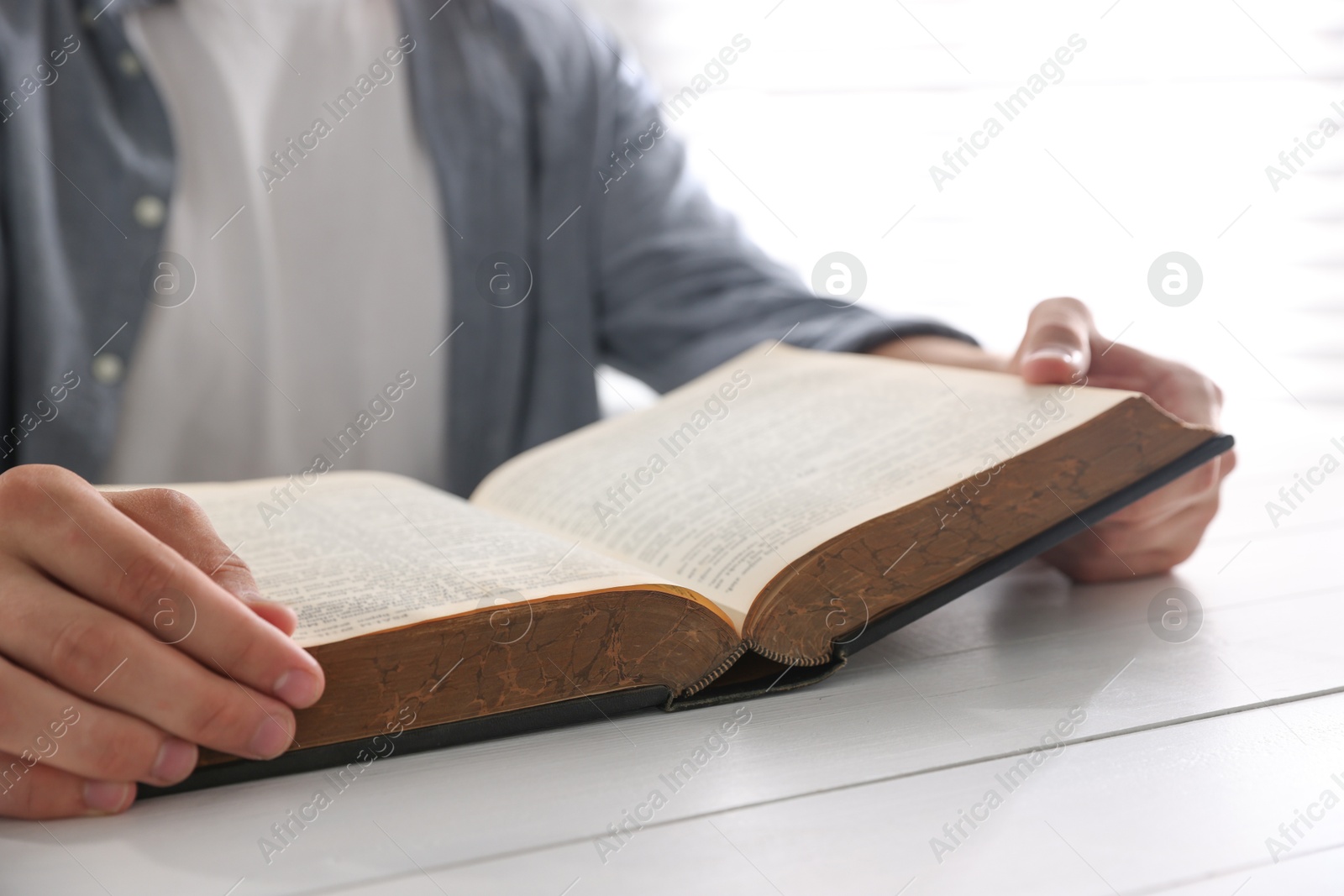 Photo of Man with Bible at white wooden table, closeup