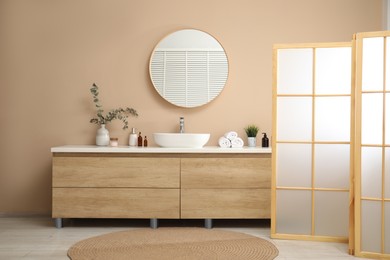 Photo of Folding screen, vanity, sink, mirror and floral decor in bathroom. Interior design