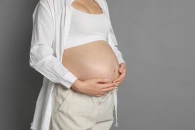 Photo of Young pregnant woman on grey background, closeup. Space for text