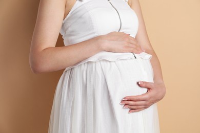 Photo of Young pregnant woman on beige background, closeup