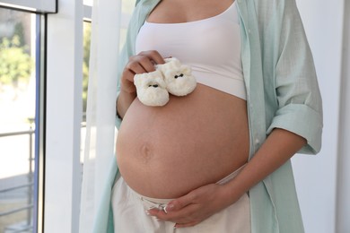 Photo of Young pregnant woman with baby shoes at home, closeup