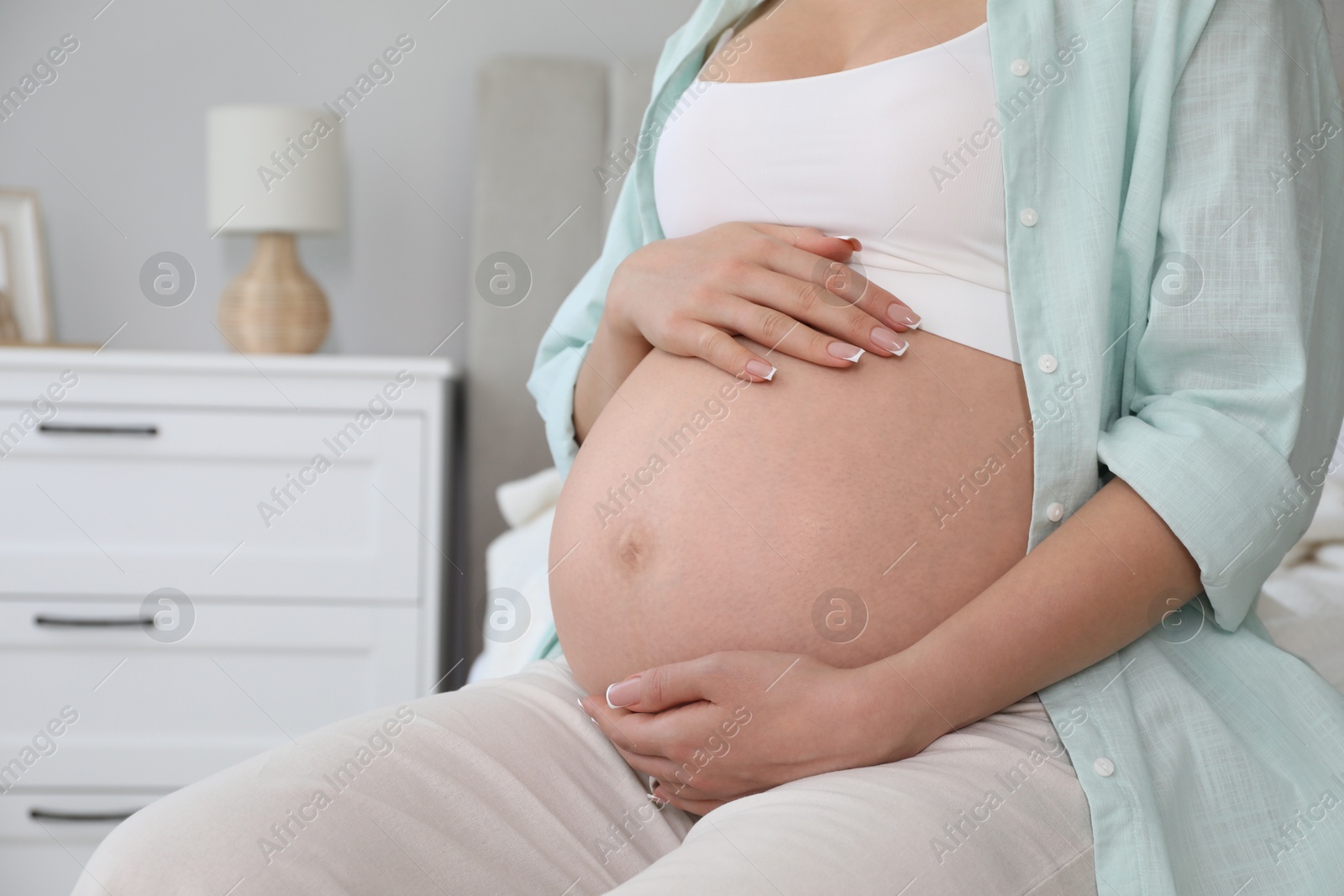 Photo of Young pregnant woman sitting on bed at home, closeup