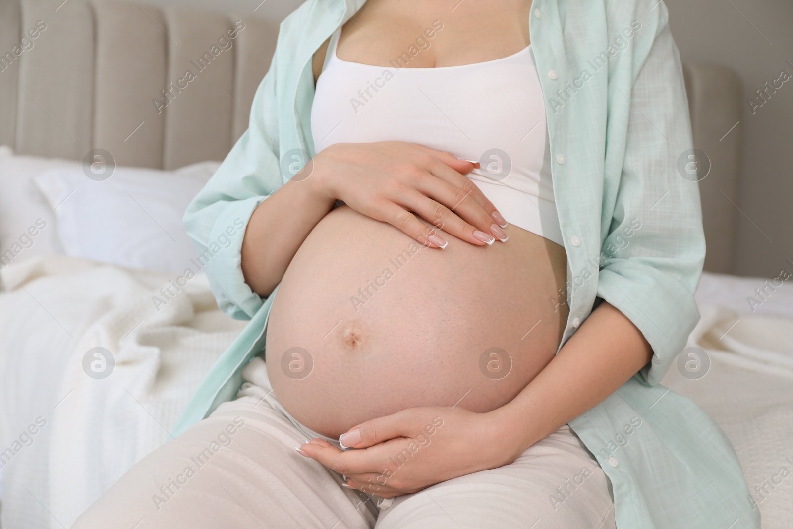 Photo of Young pregnant woman sitting on bed at home, closeup