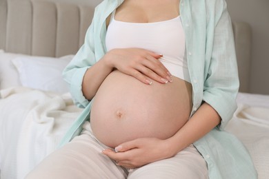 Photo of Young pregnant woman sitting on bed at home, closeup