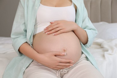 Photo of Young pregnant woman sitting on bed at home, closeup