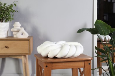 Photo of Wooden stool with knot cushion in room. Stylish interior design