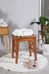 Photo of Wooden stool with knot cushion in room. Stylish interior design