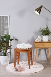 Photo of Wooden stool with knot cushion in room. Stylish interior design