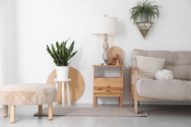 Photo of Stool, sofa, lamp and houseplants in room. Interior design