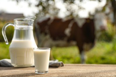 Photo of Fresh milk in jug and glass on wooden table outdoors