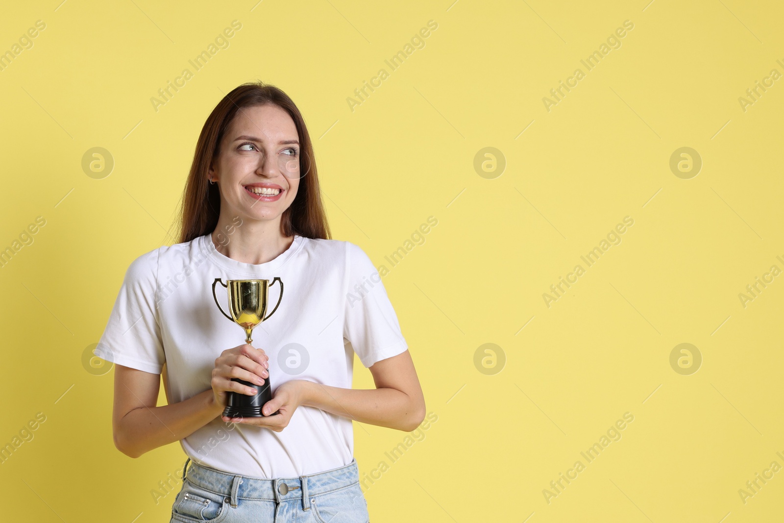 Photo of Happy winner with gold trophy cup on yellow background, space for text