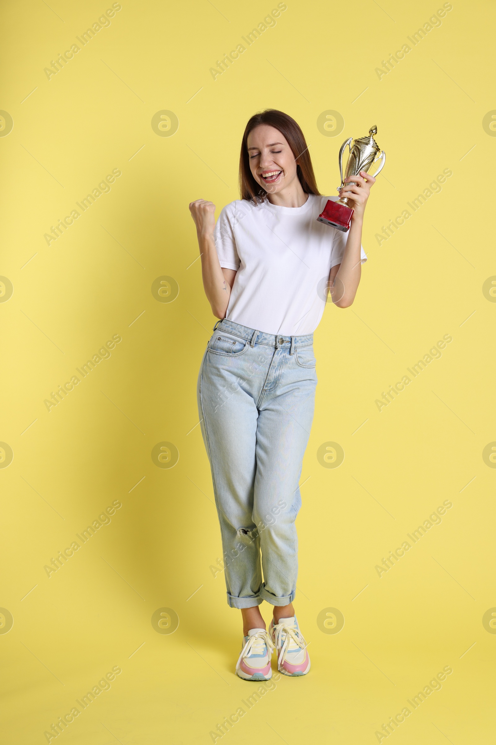 Photo of Happy winner with gold trophy cup on yellow background