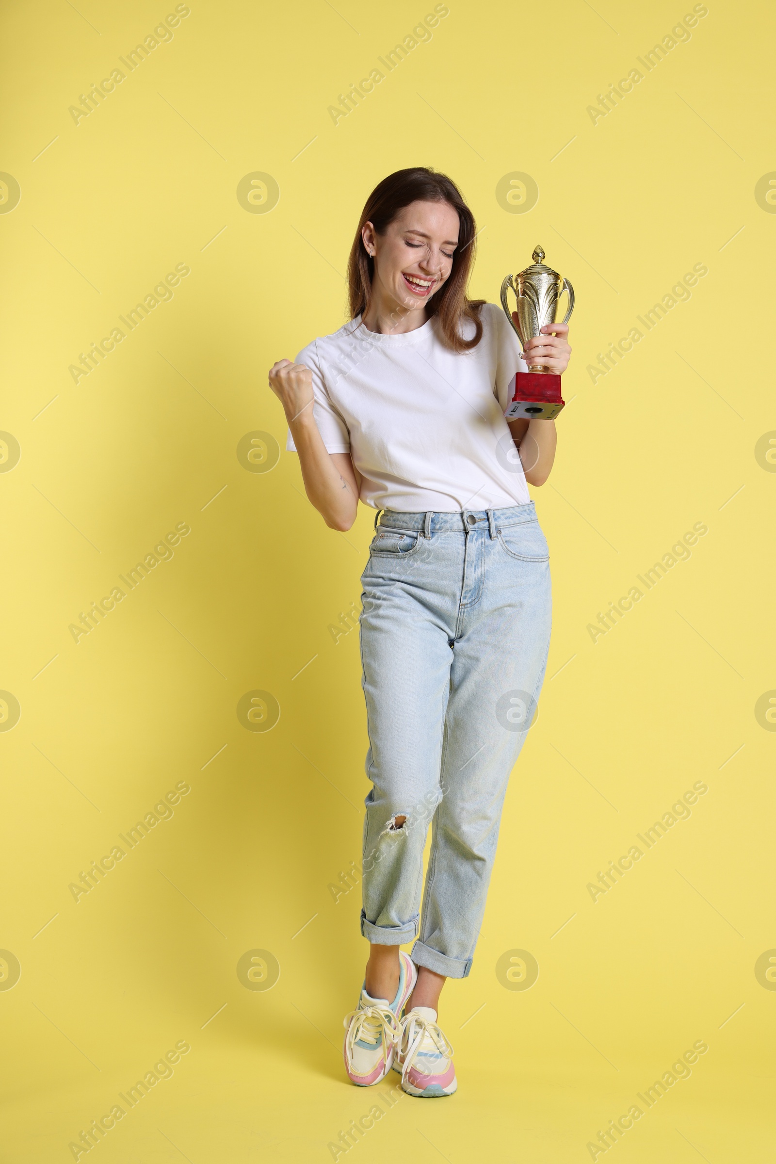 Photo of Happy winner with gold trophy cup on yellow background