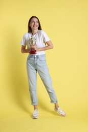 Photo of Happy winner with gold trophy cup on yellow background