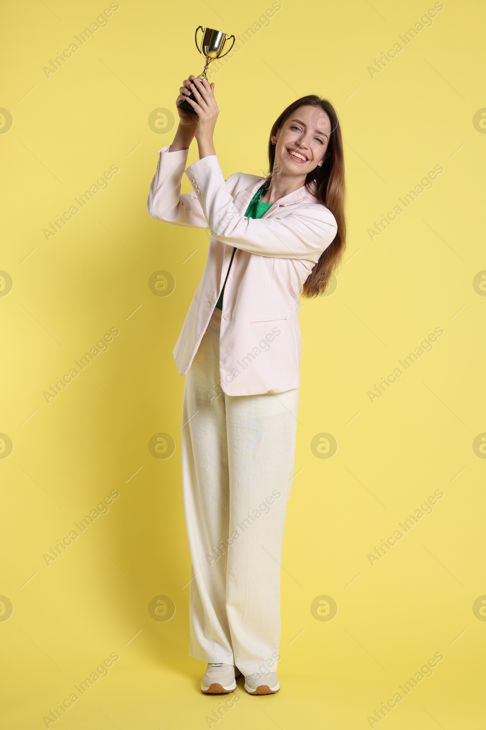 Photo of Happy winner with gold trophy cup on yellow background