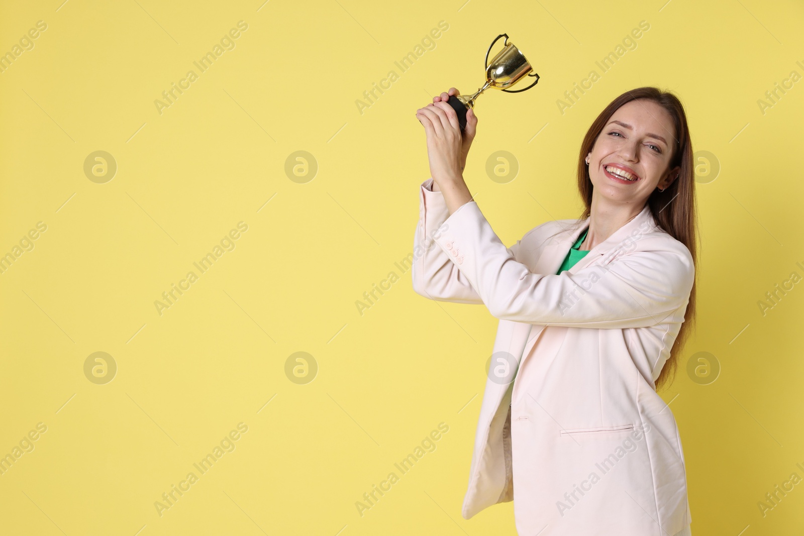 Photo of Happy winner with gold trophy cup on yellow background, space for text