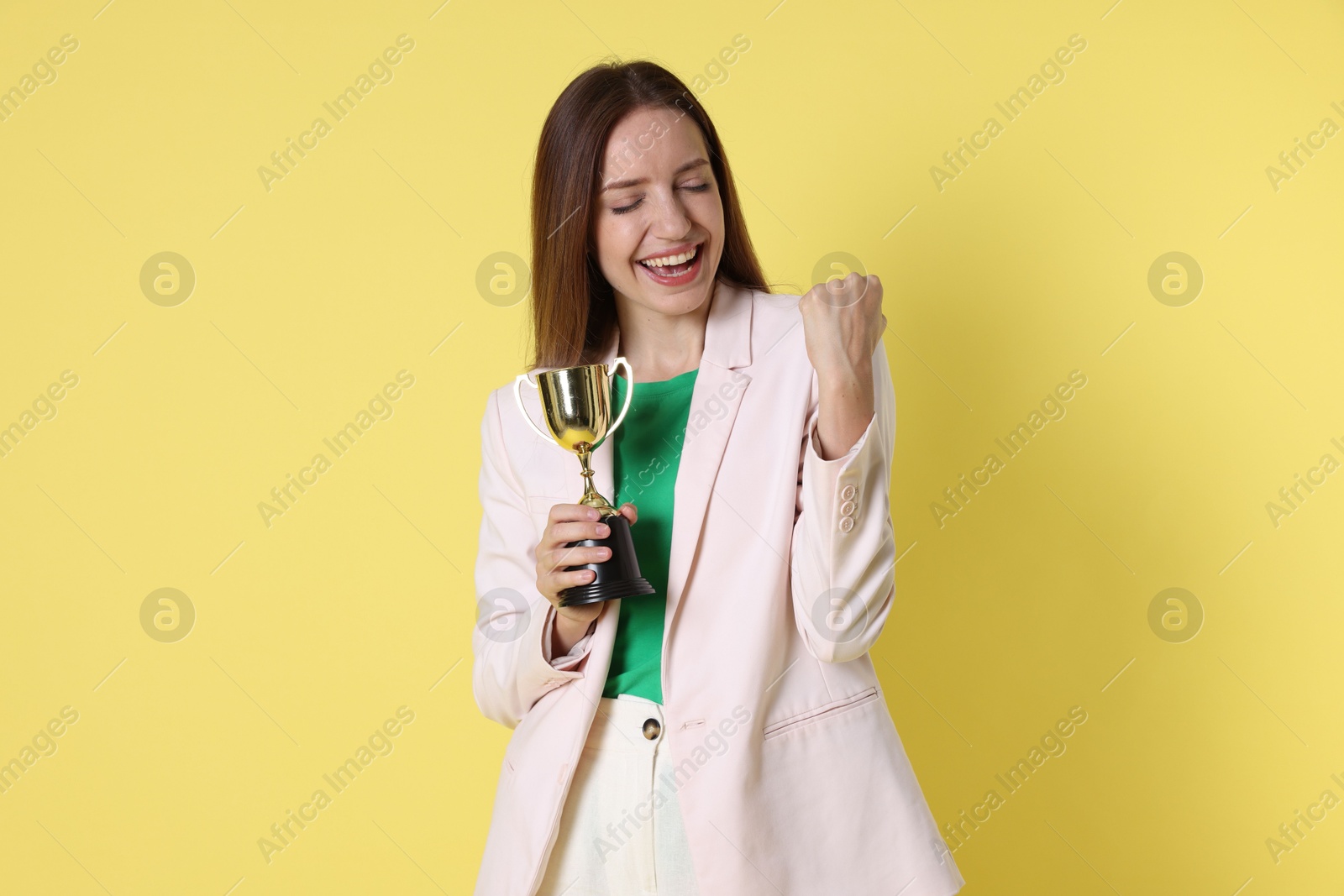 Photo of Happy winner with gold trophy cup on yellow background