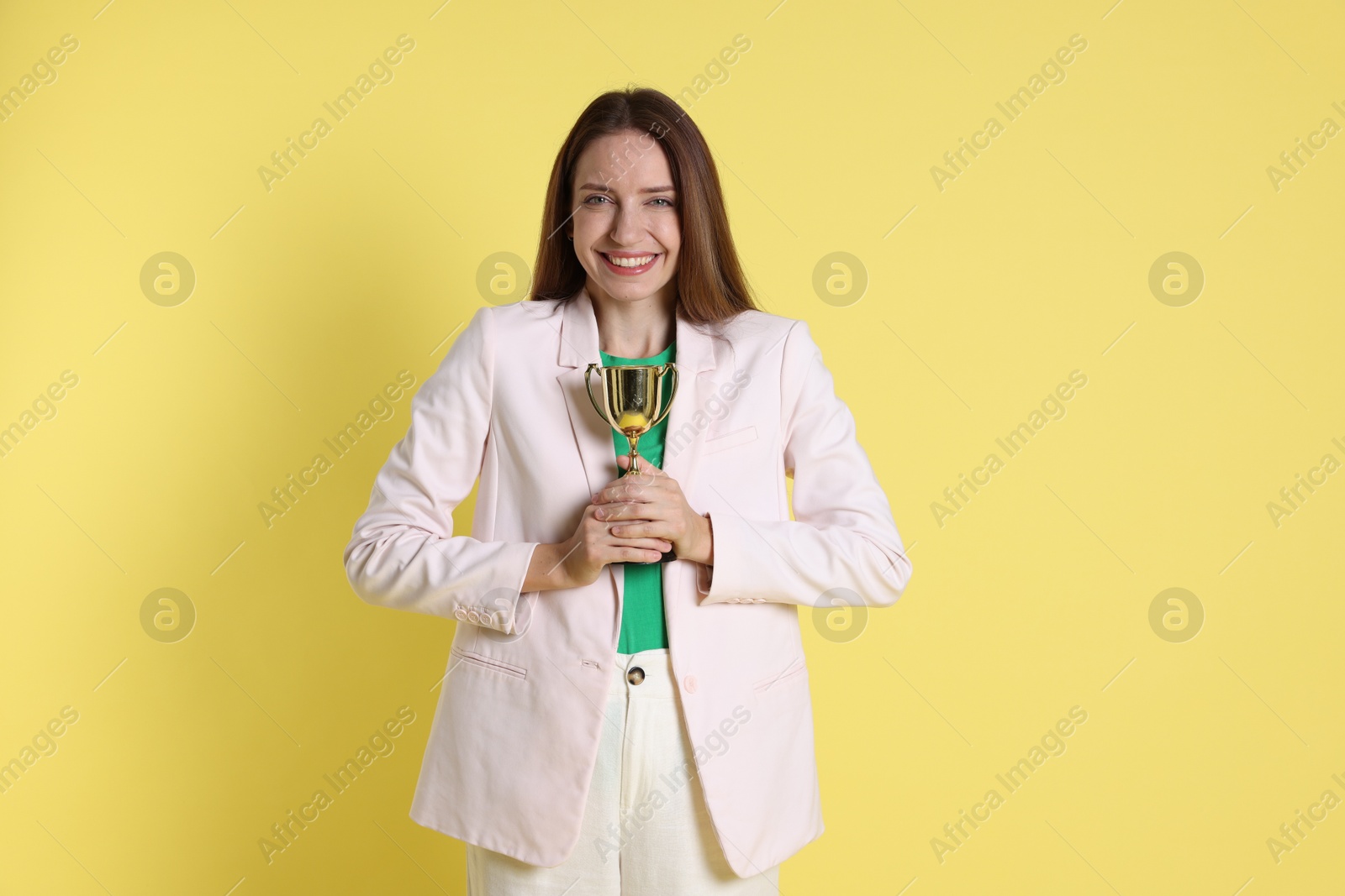 Photo of Happy winner with gold trophy cup on yellow background