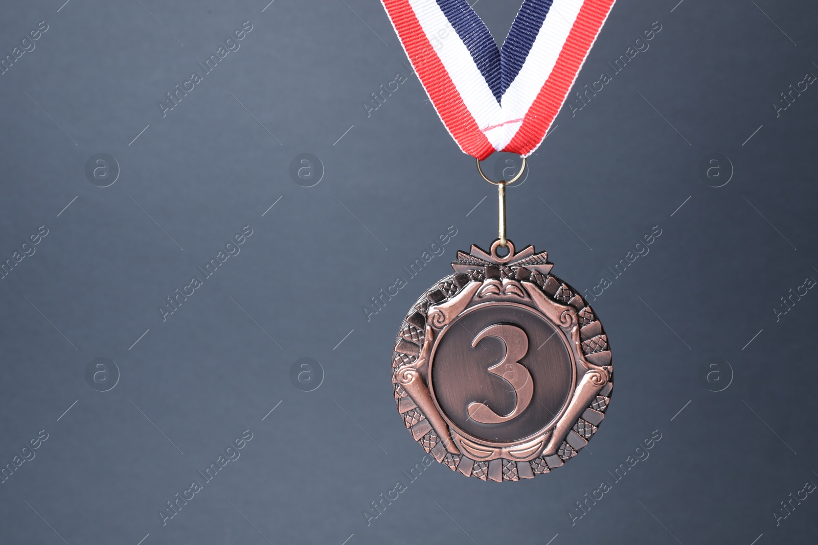 Photo of Bronze medal with striped ribbon on grey background, space for text