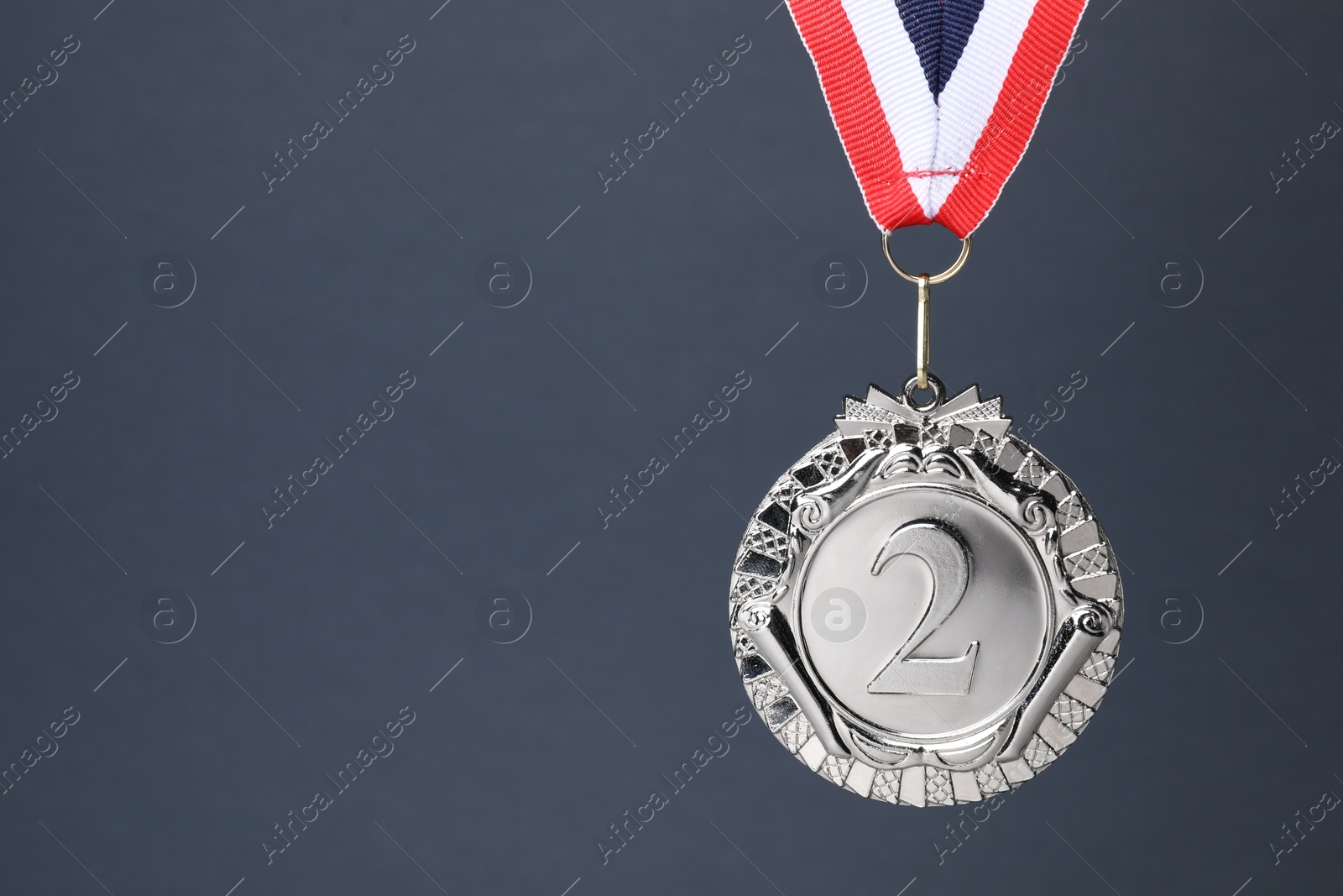 Photo of Silver medal with striped ribbon on grey background, space for text