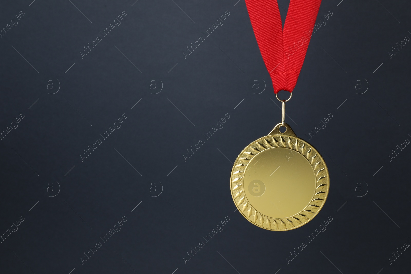 Photo of Golden medal with red ribbon on dark grey background, space for text