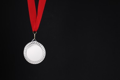 Photo of Silver medal with red ribbon on black background, space for text