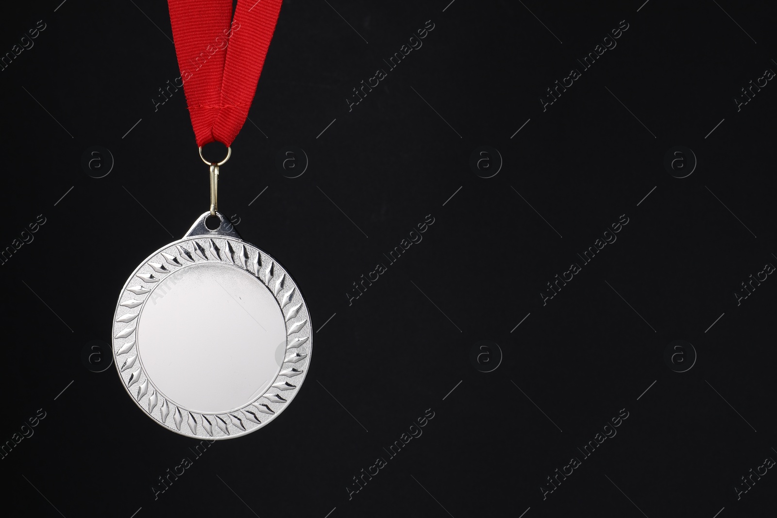 Photo of Silver medal with red ribbon on black background, space for text