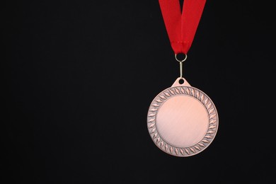 Photo of Bronze medal with red ribbon on black background, space for text