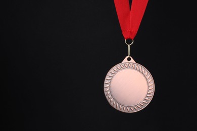 Photo of Bronze medal with red ribbon on black background, space for text