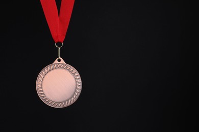 Photo of Bronze medal with red ribbon on black background, space for text