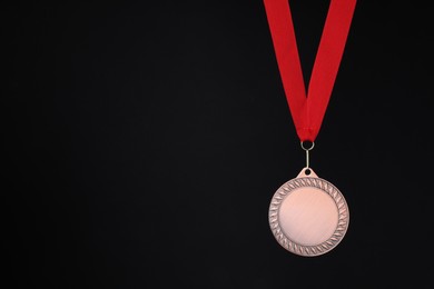 Photo of Bronze medal with red ribbon on black background, space for text