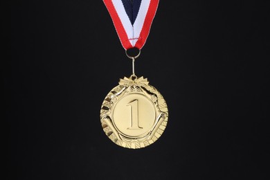 Photo of Golden medal with striped ribbon on black background