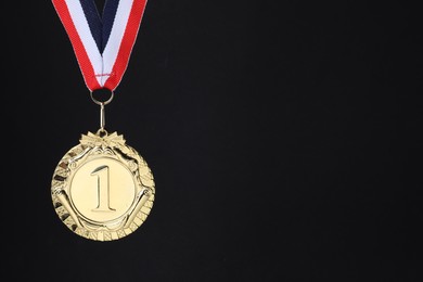 Photo of Golden medal with striped ribbon on black background, space for text