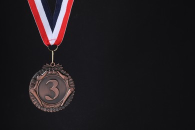 Photo of Bronze medal with striped ribbon on black background, space for text