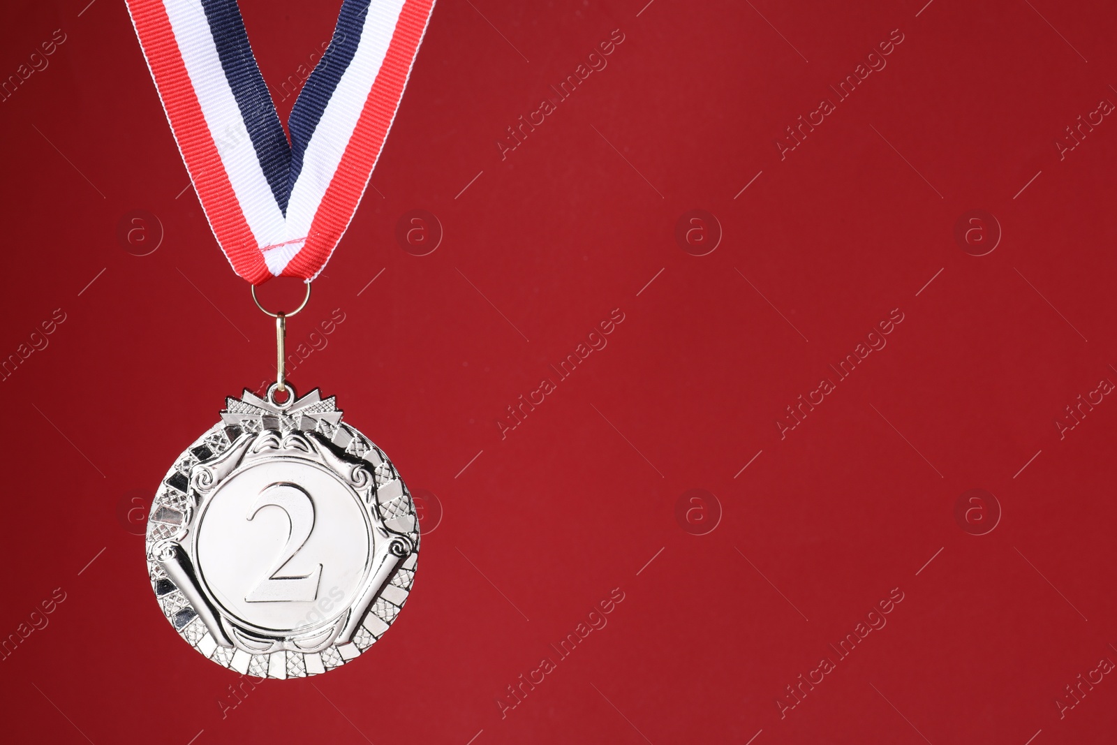 Photo of Silver medal with striped ribbon on red background, space for text