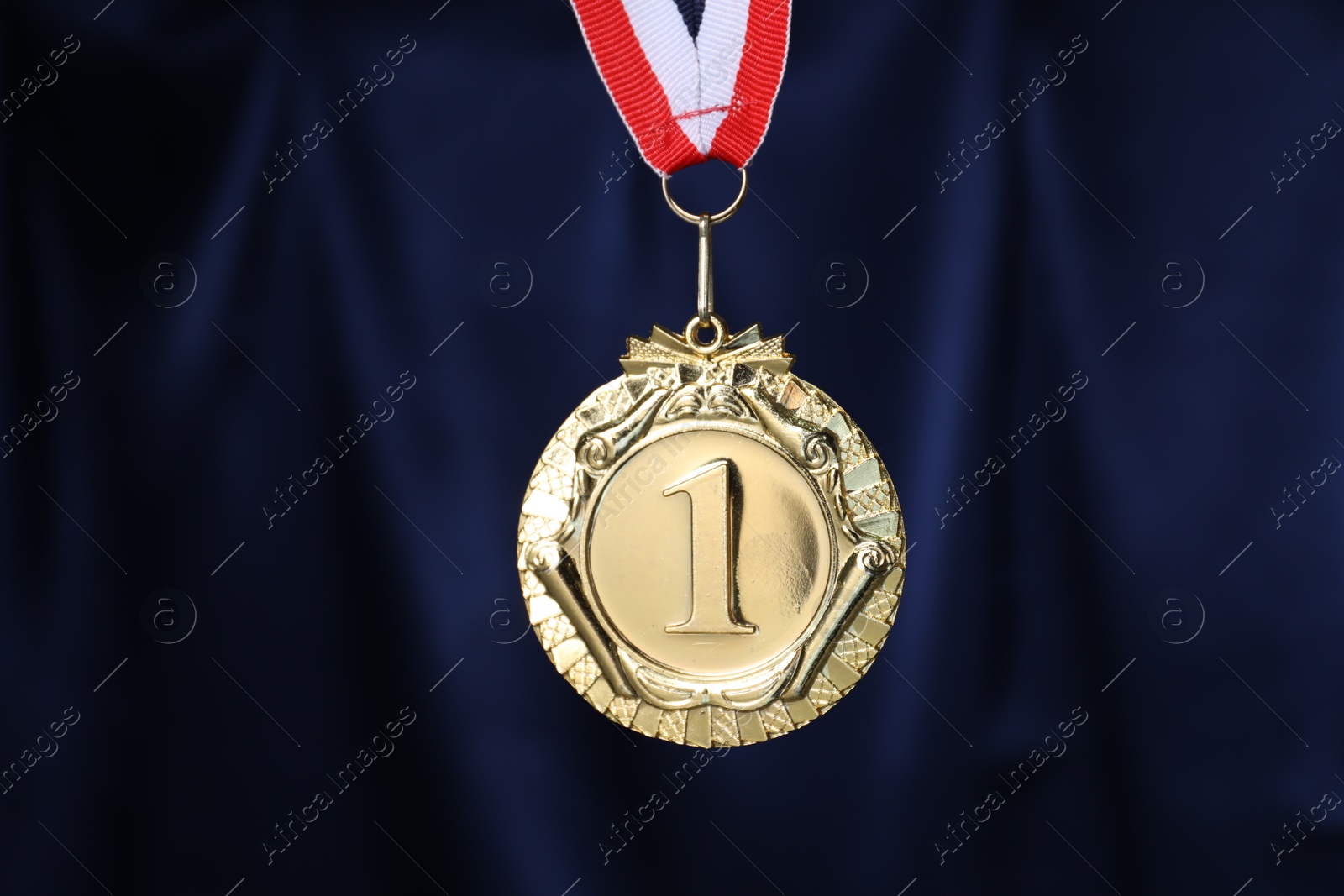 Photo of Golden medal with striped ribbon against blue fabric, closeup