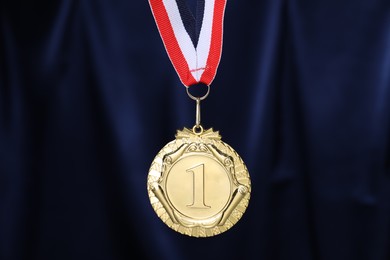 Photo of Golden medal with striped ribbon against blue fabric, closeup