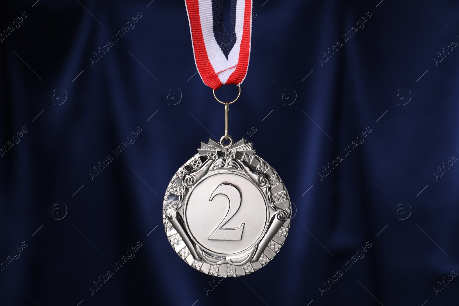 Photo of Silver medal with striped ribbon against blue fabric, closeup