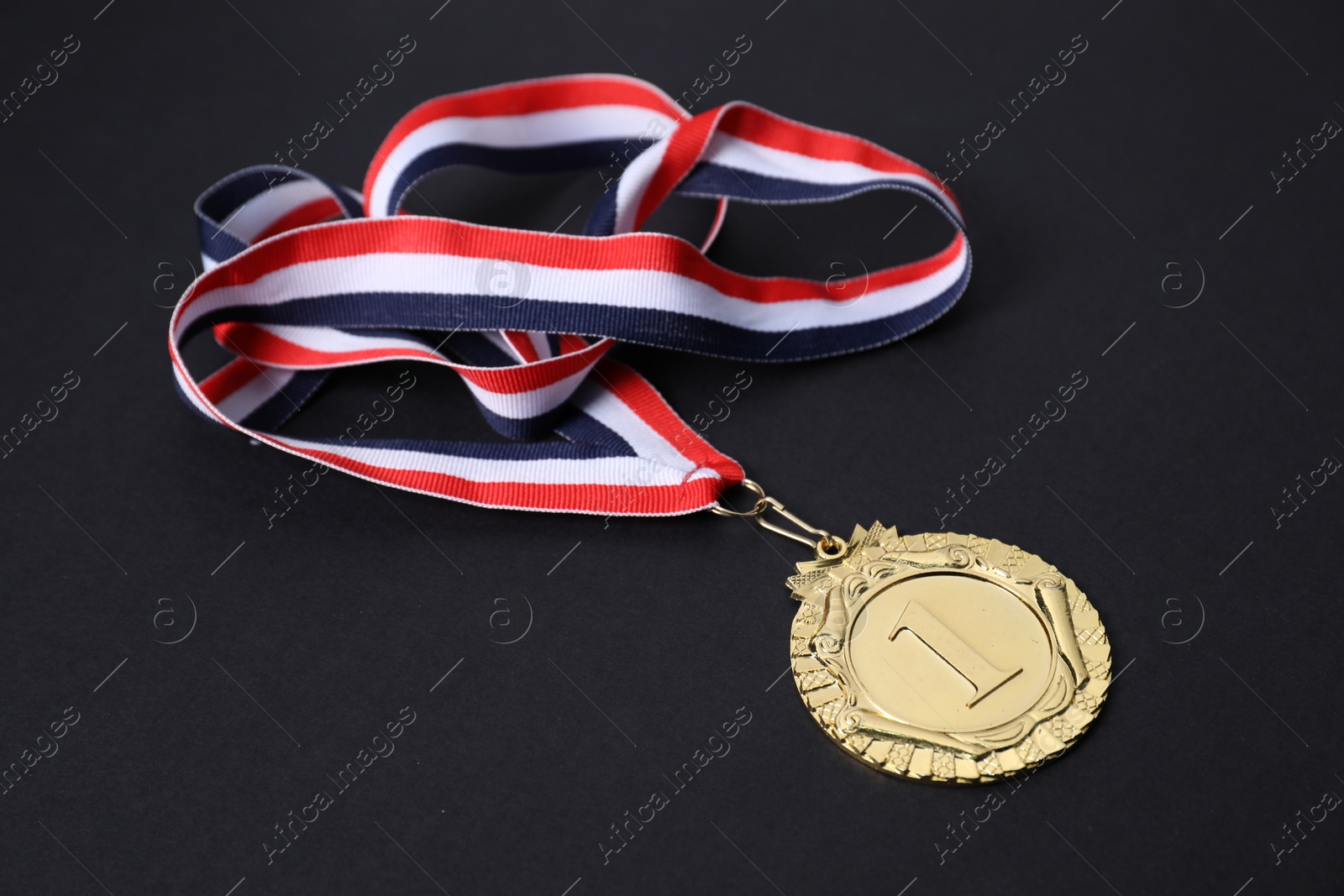 Photo of Golden medal with striped ribbon on black background, closeup