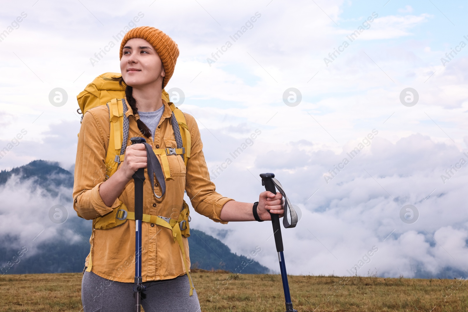 Photo of Young hiker with trekking poles and backpack in mountains outdoors, space for text